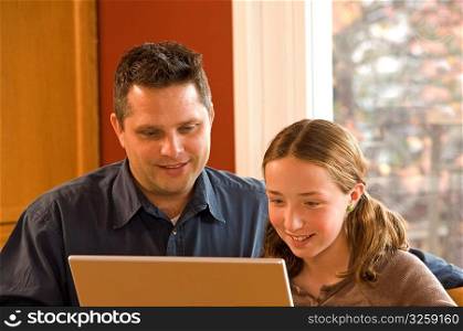 Father and daughter working on wireless laptop computer at home.
