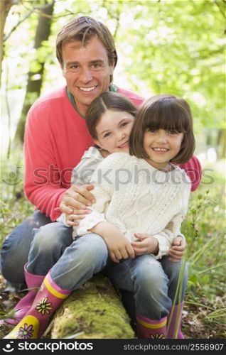 Father and daughters outdoors in woods sitting on log smiling