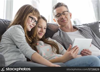 Father and daughters using tablet PC on sofa at home