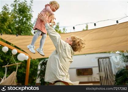 Father and gaughter play at the trailer, summer camping. Family with kids travel in camp car, nature and forest on background. Campsite adventure, travelling lifestyle. Father and gaughter play at the trailer, camping