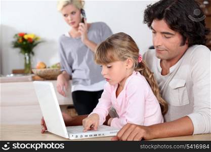 father and her daughter doing computer, mother at phone