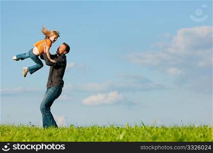 Father and his kid - daughter - playing together at a meadow, he is throwing her into the air at a late summer afternoon, family concept