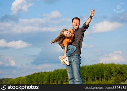 Father and his kid - daughter - playing together at a meadow, he is carrying her on his shoulders