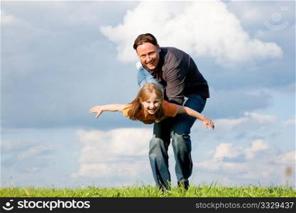 Father and his kid - daughter - playing together at a meadow, he is carrying her on his hands