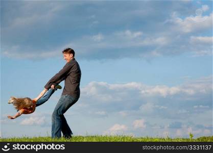 Father and his kid - daughter - playing together at a meadow, he is tossing her around