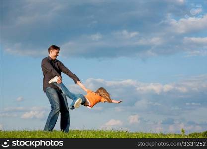 Father and his kid - daughter - playing together at a meadow, he is tossing her around