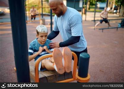 Father and kid doing exercise, sport training on playground outdoors. The family leads a healthy lifestyle, fitness workout in summer park. Father and kid doing exercise, sport training