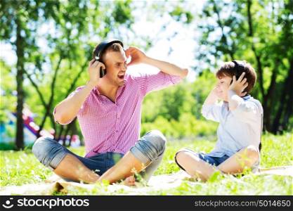 Father and kid in summer park enjoying music. Weekend in park