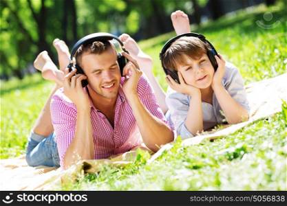 Father and kid in summer park enjoying music. Weekend in park