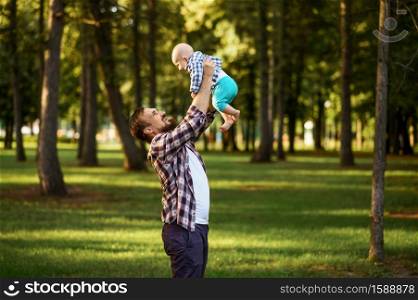 Father and little baby walks in summer park. Dad with male kid on lawn, picnic with child on plaid in the forest, family happiness. Father and little baby walks in park