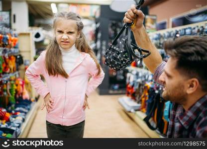 Father and little daughter buying muzzle in pet shop. Family chooses accessories for dog in petshop