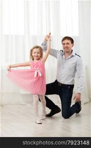 Father and little daughter dancing. Little princess in pink dress walking around dad standing on knee. Little princess dancing with father