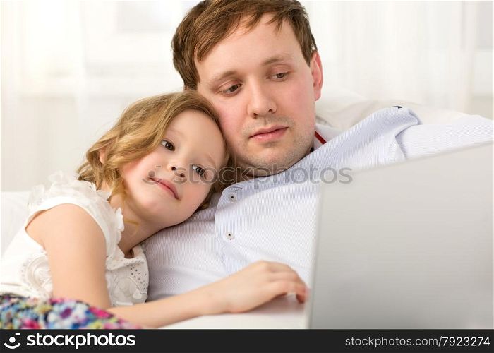 Father and little daughter on the sofa at home. Father holding laptop, girl using it leaning on dads shoulder