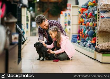 Father and little dauther are plays with puppy in pet shop. Family buying supplies for little dog in petshop. Father and dauther plays with puppy in pet shop