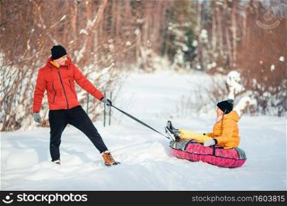 Father and little girl riding on a tube and having fun outdoors in winter. Family of dad and kids vacation on Christmas eve outdoors