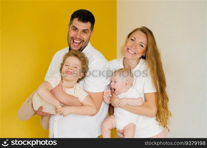 Father and mother stand side by side on a yellow background and hold the brothers’ children in their arms. a man and a woman are happy with their family