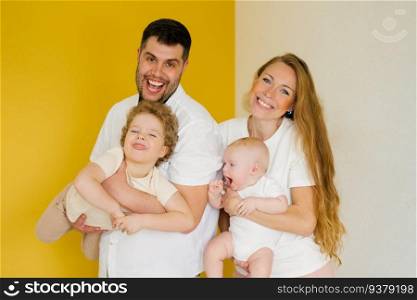 Father and mother stand side by side on a yellow background and hold the brothers’ children in their arms. a man and a woman are happy with their family