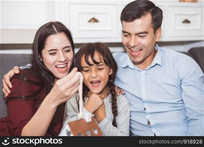 Father and mother surprise their daughter by gift or new toy. Parents and children are happy together in home on sofa in living room. Family and Happiness of life concept.