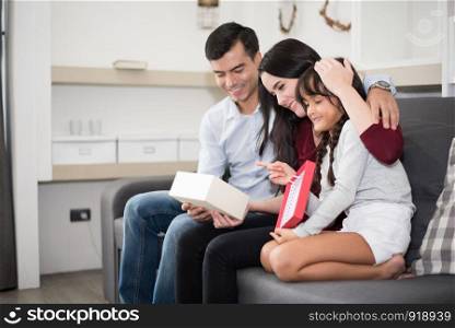 Father and mother surprise their daughter by gift or new toy. Parents and children are happy together in home on sofa. Family and Happiness concept.