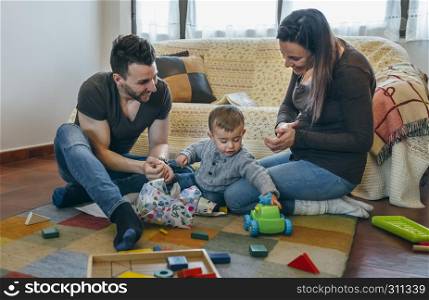 Father and pregnant mother with their little son opening a gift in the living room. Parents with their little son opening a gift