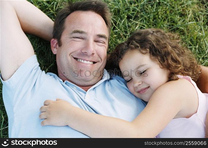 Father and sleeping daughter lying outdoors smiling