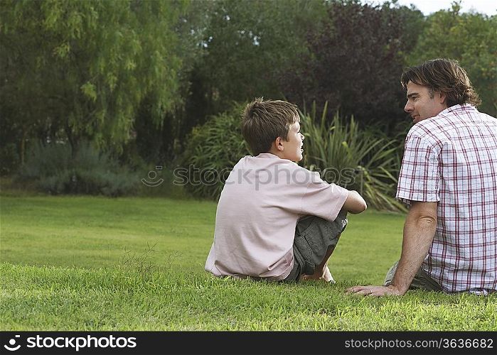 Father and son (10-12) sitting on lawn and talking