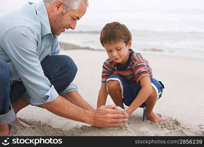 Father and son (5-6) playing in sand on beach