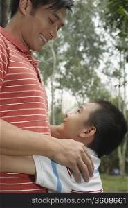 Father and son (7-9) in park, embracing and looking in eyes