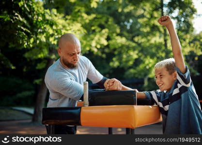 Father and son, arm wrestling exercise, sport training on playground outdoors. The family leads a healthy lifestyle, fitness workout in summer park. Father and son, arm wrestling exercise, playground