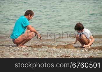 Father and son builds sandcastle on the summer beach