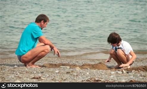 Father and son builds sandcastle on the summer beach