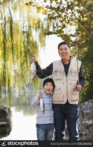 Father and son displaying fishing catch at lake