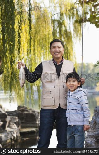 Father and son displaying fishing catch at lake