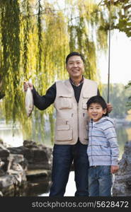 Father and son displaying fishing catch at lake