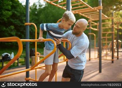 Father and son doing exercise, sport training on playground outdoors. The family leads a healthy lifestyle, fitness workout in summer park. Father and son doing exercise, sport training