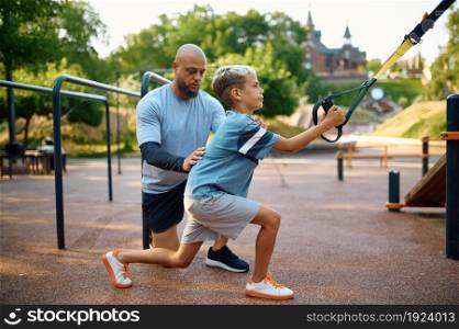 Father and son, exercise with ropes, sport training on playground outdoors. The family leads a healthy lifestyle, fitness workout in summer park. Father and son, exercise with ropes on playground