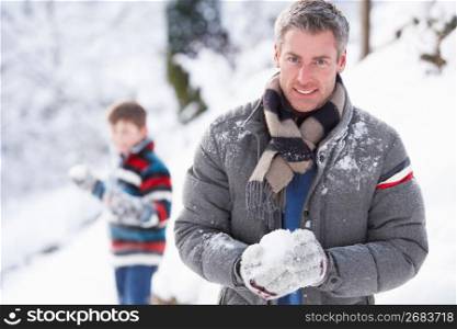 Father And Son Having Snowball Fight In Winter Landscape