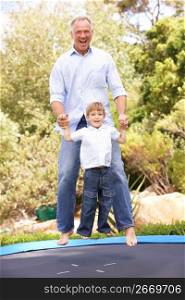 Father And Son Jumping On Trampoline In Garden