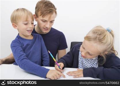 Father and son looking at girl studying at table