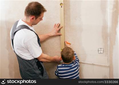 Father and son measuring a dry wall in their home with a folding rule and a bubble level