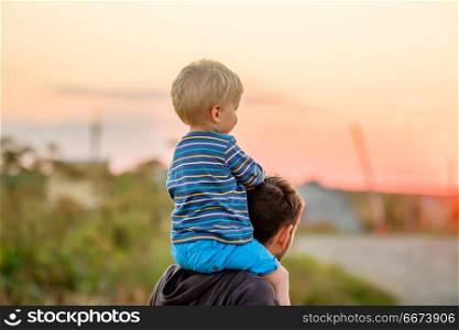 Father and son outdoor portrait in sunset sunlight. Happy man and his child having fun outdoors. Family lifestyle rural scene of father and son in sunset sunlight.