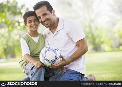Father and son outdoors in park with ball smiling (selective focus)