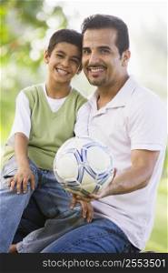 Father and son outdoors in park with ball smiling (selective focus)