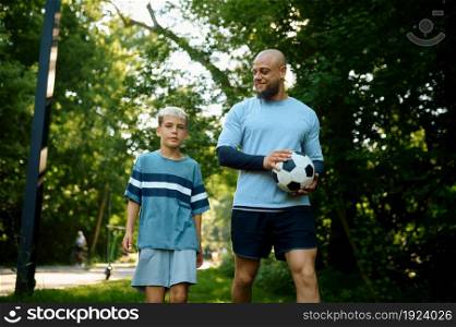 Father and son play football on sunny day outdoors . The family leads a healthy lifestyle, morning fitness workout in summer park. Father and son play football on sunny day