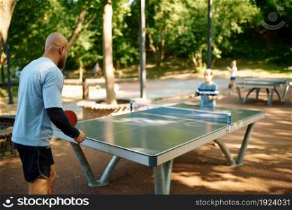 Father and son play table tennis outdoors. The family leads a healthy lifestyle, daddy and boy, ping pong training in summer park. Father and son play table tennis outdoors