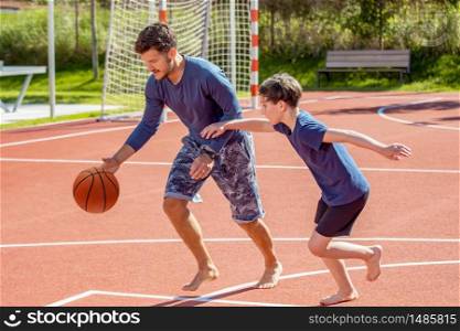 Father and son playing basketball barefoot on a playground