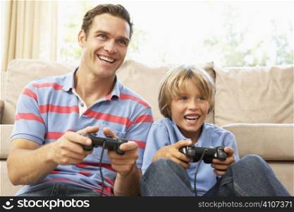Father And Son Playing Computer Game On Sofa At Home
