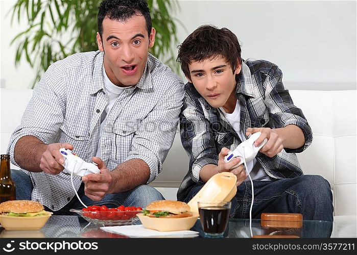 Father and son playing computer games and eating junk food
