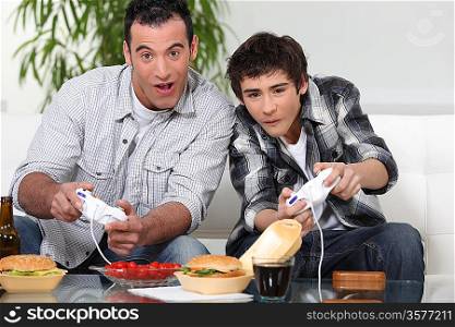 Father and son playing computer games and eating junk food