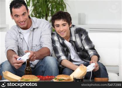 Father and son playing video games whilst eating fast-food